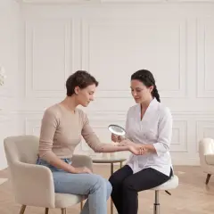 Kosmetolog bada znamiona na ręce pacjentki, przygotowując się do zabiegu elektrokoagulacji.